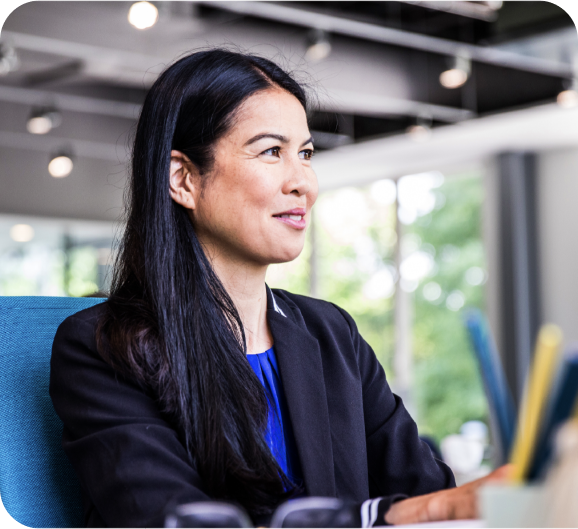 A smiling woman in a black suit sitting at her office desk
